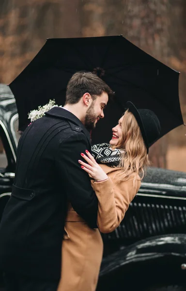 Gorgeous newlywed bride and groom posing in pine forest near retro car in their wedding day — 图库照片