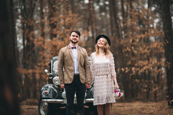 Magnifique jeune marié mariée et marié posant dans la forêt de pins près de voiture rétro dans leur jour de mariage — Photo