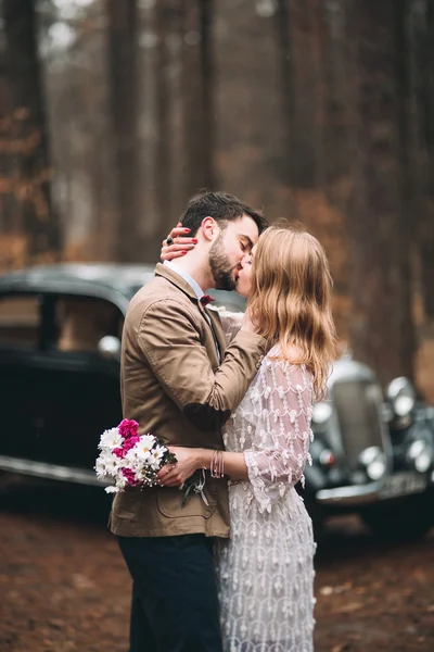 Hermosa novia recién casada y novio posando en un bosque de pinos cerca de coche retro en el día de su boda —  Fotos de Stock