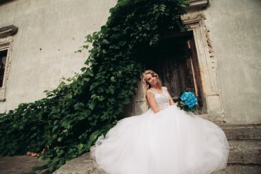 Güzel genç sarışın gelin gelin buketi muhteşem bitkiler altında merdivenlerde oturan ile