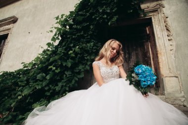 Güzel genç sarışın gelin gelin buketi muhteşem bitkiler altında merdivenlerde oturan ile