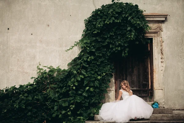 Belle jeune mariée blonde avec bouquet nuptiale assise dans les escaliers sous de magnifiques plantes — Photo