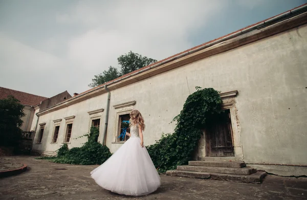 Bella giovane sposa bionda con bouquet da sposa seduta sulle scale sotto splendide piante — Foto Stock