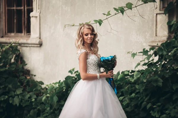 Belle jeune mariée blonde avec bouquet nuptiale assise dans les escaliers sous de magnifiques plantes — Photo