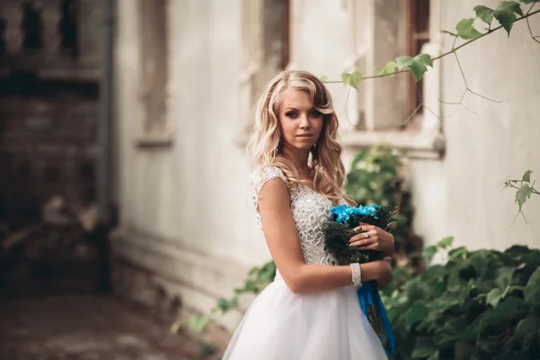 Bella giovane sposa bionda con bouquet da sposa seduta sulle scale sotto splendide piante — Foto Stock