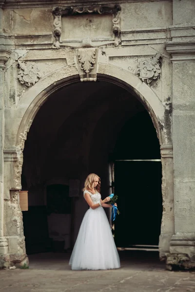 Schöne junge blonde Braut mit Brautstrauß sitzt auf der Treppe unter wunderschönen Pflanzen — Stockfoto