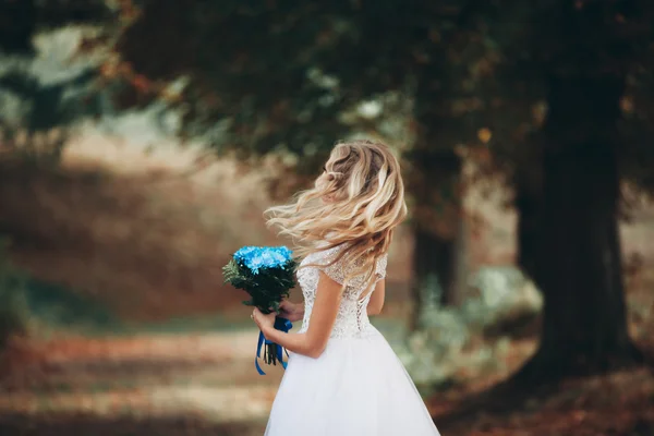 Beautiful young blond bride with bridal bouquet sitting on the stairs under gorgeous plants — Stock Photo, Image