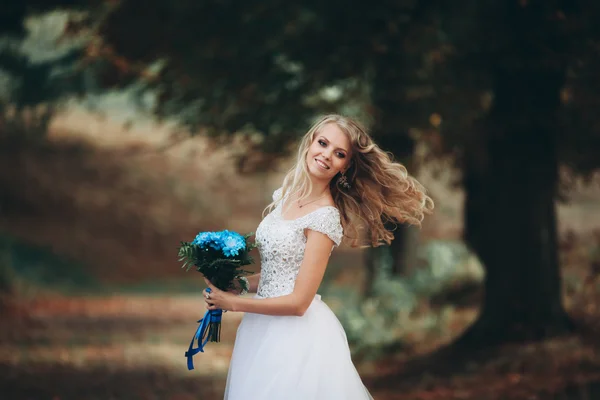 Beautiful young blond bride with bridal bouquet sitting on the stairs under gorgeous plants — Stock Photo, Image