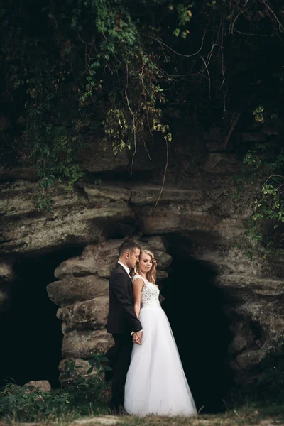 Pareja de boda de lujo abrazos y besos en el fondo hermosas plantas y cueva cerca del antiguo castillo —  Fotos de Stock