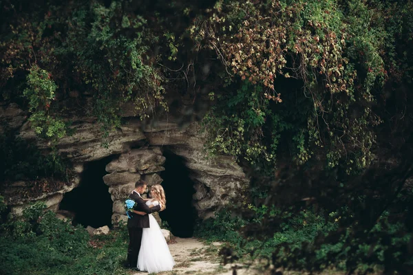 Πολυτελές γαμήλιο ζευγάρι αγκάλιασμα και το φίλημα στα πανέμορφα φυτά φόντο και σπήλαιο κοντά στο αρχαίο κάστρο — Φωτογραφία Αρχείου