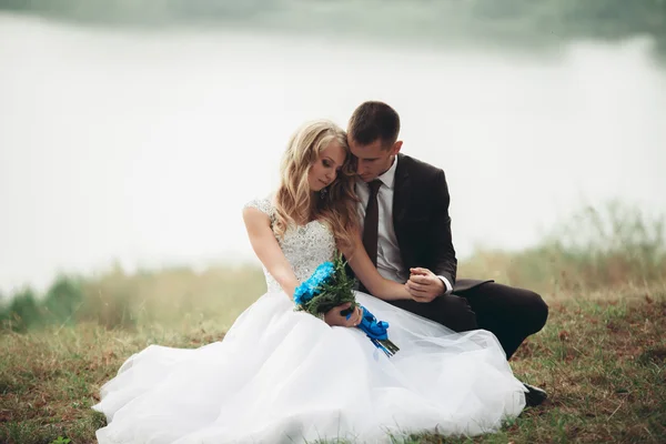 Happy wedding couple sitting on the ground near the lake — Stock Photo, Image