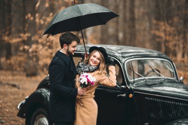 Şık Loving düğün çift öpüşme ve retro car yakınındaki bir çam ormanı içinde sarılma