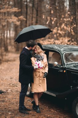 Şık Loving düğün çift öpüşme ve retro car yakınındaki bir çam ormanı içinde sarılma