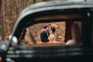 Şık Loving düğün çift öpüşme ve retro car yakınındaki bir çam ormanı içinde sarılma