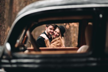 Şık Loving düğün çift öpüşme ve retro car yakınındaki bir çam ormanı içinde sarılma