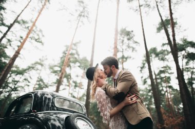 Şık Loving düğün çift öpüşme ve retro car yakınındaki bir çam ormanı içinde sarılma