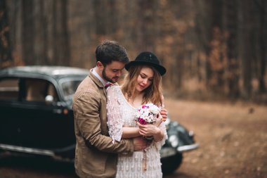 Şık Loving düğün çift öpüşme ve retro car yakınındaki bir çam ormanı içinde sarılma