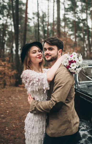Κομψό ζευγάρι γάμος αγάπη φιλί και αγκαλιάζει σε ένα πευκοδάσος κοντά αυτοκίνητο ρετρό — Φωτογραφία Αρχείου