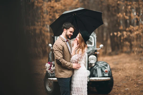 スタイリッシュな愛する結婚式のカップルのキスとハグ レトロな車の近くの松林の中 — ストック写真