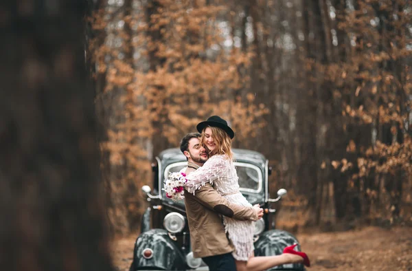 Elegante coppia di nozze amorevole baciare e abbracciare in una pineta vicino auto retrò — Foto Stock