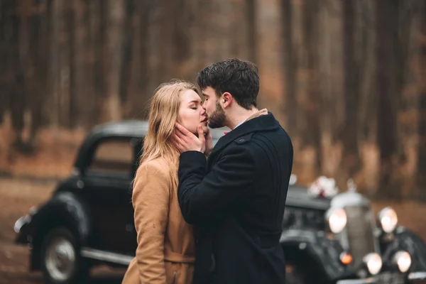 Eleganta Loving bröllop par kyssar och kramar i en pinjeskog nära retro bil — Stockfoto