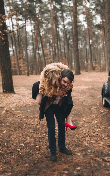 Elegante pareja de boda cariñosa besándose y abrazándose en un bosque de pinos cerca de coche retro —  Fotos de Stock