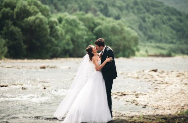 Zarif nazik şık damat ve gelin taşlarla Nehri yakınında. Evlilik çift aşık