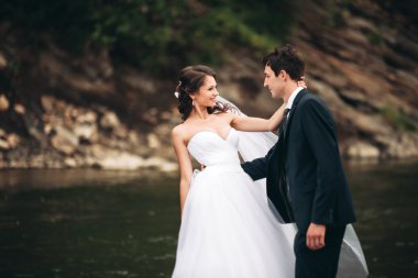 Güzel düğün çifti bir dağ nehrinin kıyısında taşlarla öpüşüp kucaklaşıyorlar.