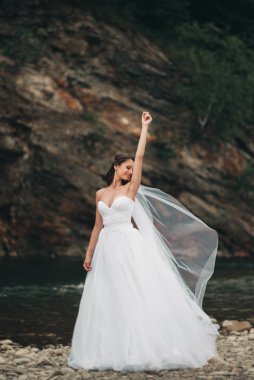 Uzun beyaz gelinlik ve peçe dağlar arka plan üzerinde Nehri yakınında duran güzel lüks genç gelin