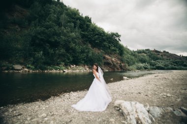 Uzun beyaz gelinlik ve peçe dağlar arka plan üzerinde Nehri yakınında duran güzel lüks genç gelin