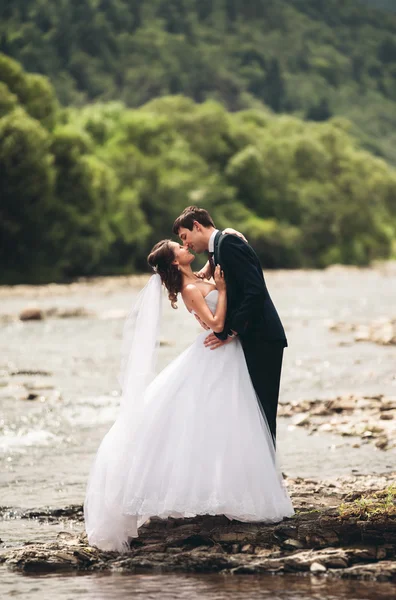 Élégant marié élégant doux et la mariée près de la rivière avec des pierres. Couple de mariage amoureux — Photo