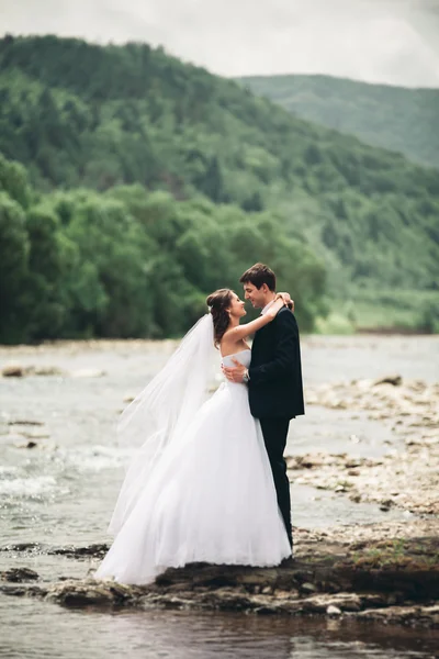 Elegante gentile sposo elegante e sposa vicino al fiume con pietre. Matrimonio coppia innamorata — Foto Stock