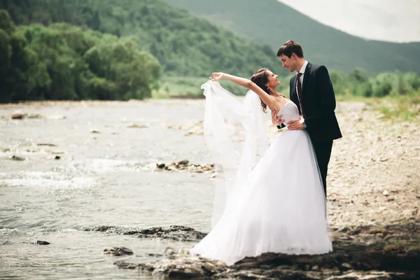 Красивая свадебная пара целуется и обнимается у берега горной реки с камнями — стоковое фото