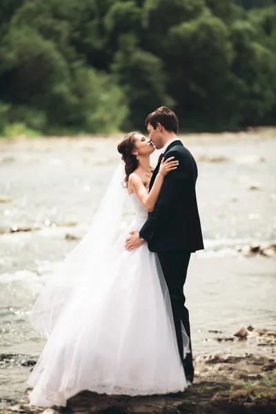 Bellissimo matrimonio coppia baciare e abbracciare vicino alla riva di un fiume di montagna con pietre — Foto Stock