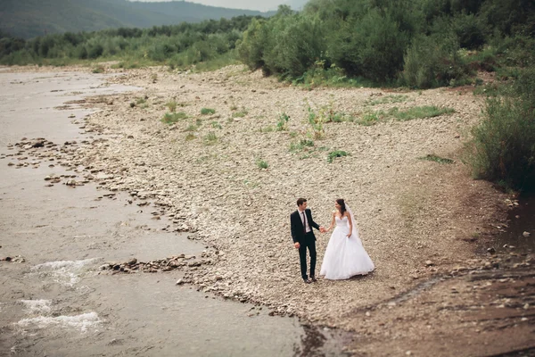 Bellissimo matrimonio coppia baciare e abbracciare vicino alla riva di un fiume di montagna con pietre — Foto Stock