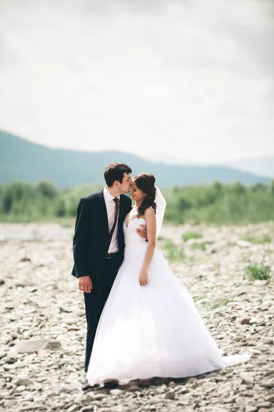 Casamento lindo casal beijando e abraçando perto da costa de um rio de montanha com pedras — Fotografia de Stock