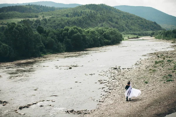 Elegante novio elegante y elegante novia cerca del río con piedras. Pareja de boda enamorada —  Fotos de Stock