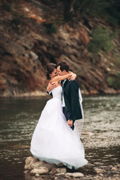 Magnifique couple de mariage embrasser et embrasser près de la rive d'une rivière de montagne avec des pierres — Photo