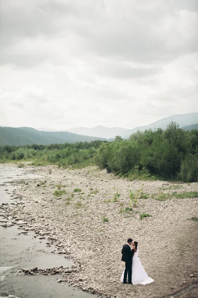 Elegante novio elegante y elegante novia cerca del río con piedras. Pareja de boda enamorada —  Fotos de Stock