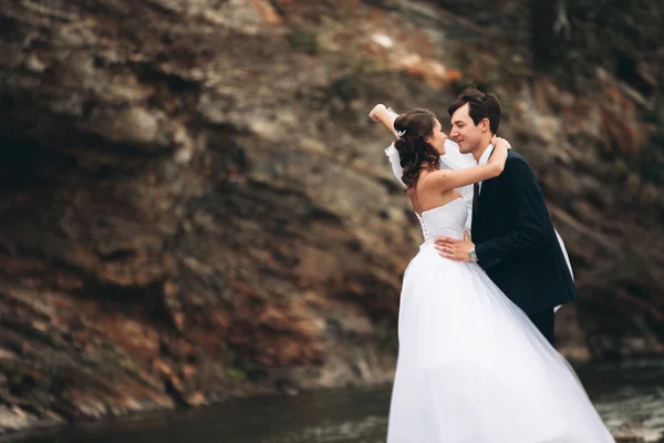 Magnifique couple de mariage embrasser et embrasser près de la rive d'une rivière de montagne avec des pierres — Photo