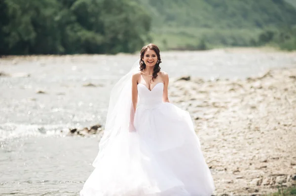 Wymarzona luksusowa panna młoda w długie, białe ślubne sukni i welonu stojący w pobliżu rzeki z góry na tle — Zdjęcie stockowe