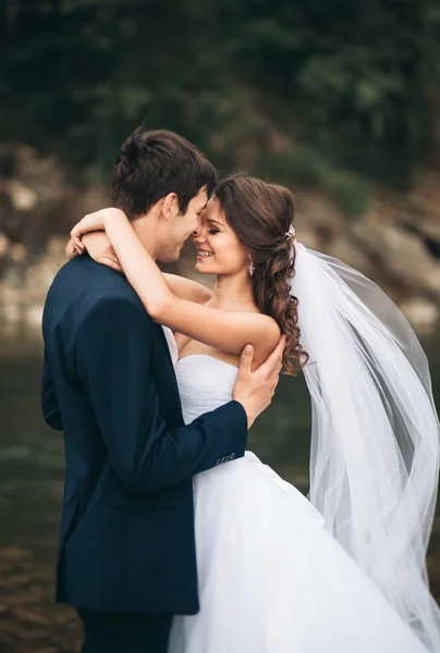 Prachtig bruidspaar zoenen en omhelzen bij de oever van een bergrivier met stenen — Stockfoto