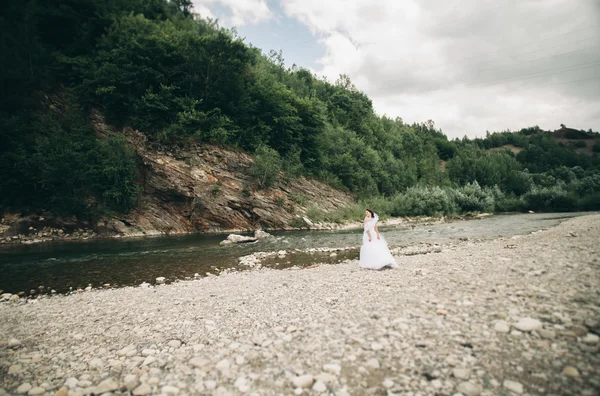 Wymarzona luksusowa panna młoda w długie, białe ślubne sukni i welonu stojący w pobliżu rzeki z góry na tle — Zdjęcie stockowe