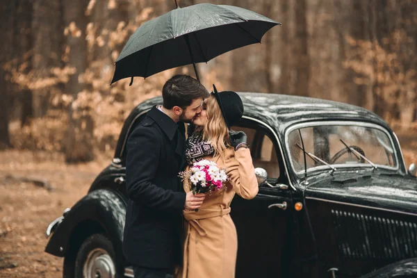 Bajki romantyczny ślub para całuje i obejmując w sosnowym lesie w pobliżu retro samochodów. — Zdjęcie stockowe