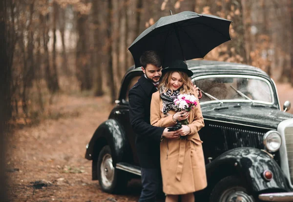 浪漫的童话婚礼情侣接吻和拥抱在松树林附近复古车. — 图库照片