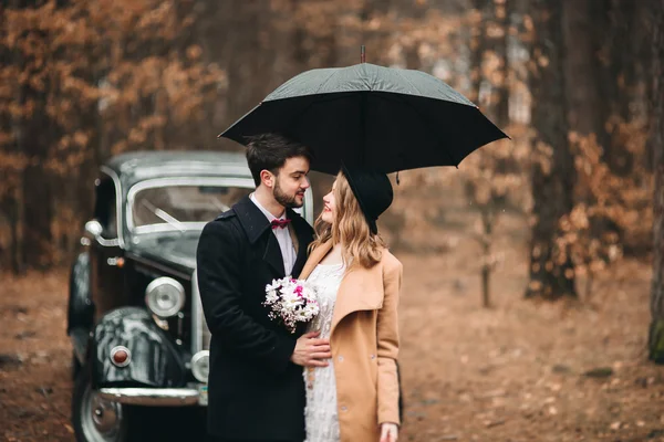 Romantik masal düğün çift öpüşme ve retro car yakınındaki çam ormanı içinde kucaklayan.