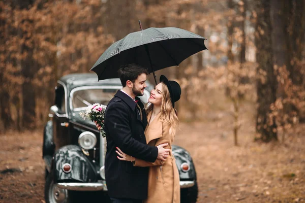 Romantik masal düğün çift öpüşme ve retro car yakınındaki çam ormanı içinde kucaklayan.
