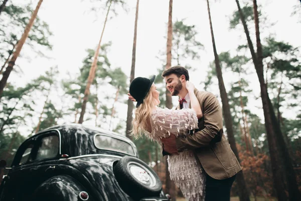 Casal de conto de fadas romântico casal beijando e abraçando na floresta de pinheiros perto de carro retro . — Fotografia de Stock