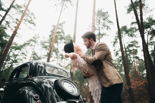 Romantická pohádka Svatební pár líbat a objímat v borovém lese poblíž retro auta. — Stock fotografie