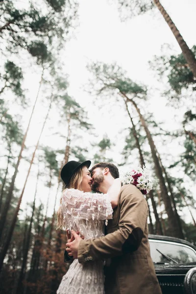 Romantik masal düğün çift öpüşme ve retro car yakınındaki çam ormanı içinde kucaklayan.
